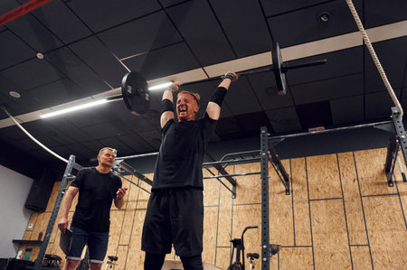 Trying hard facial expression. Strong man is lifting barbell in the gym.