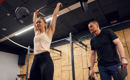 With personal male trainer. Woman is lifting barbell in the gym.