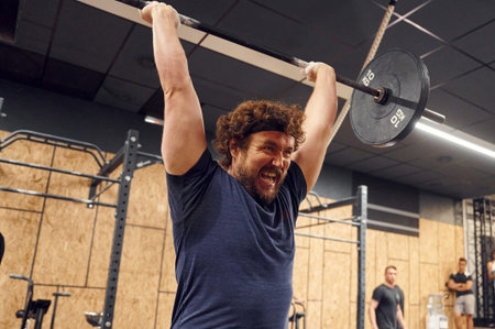 Practicing process. Strong man is lifting barbell in the gym.