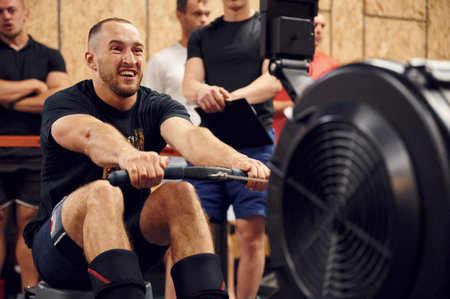 Sportive man doing exercises on rowing machine in the gym.