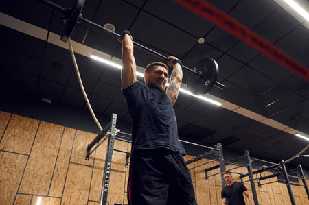 Trying hard facial expression. Strong man is lifting barbell in the gym.