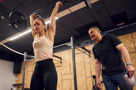 With personal male trainer. Woman is lifting barbell in the gym.