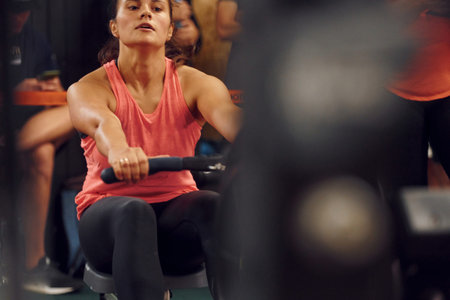 Front view. Sportive woman doing exercises on rowing machine in the gym.