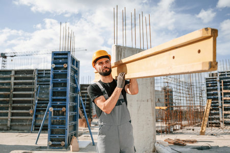 Carrying wooden plank. Man in uniform is working on the construction site.