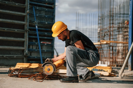 Sitting and cutting metal pieces by grinding machine. Man in uniform is working on the construction site.の写真素材