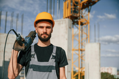 Portrait of man that is in uniform with the drill on the construction site.