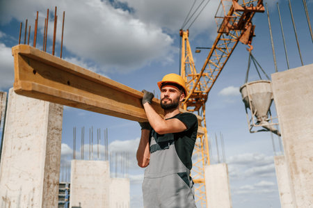 Front view of man that is in uniform holding wooden plank on the construction site.