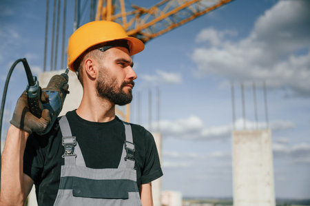 Portrait of man that is in uniform with the drill on the construction site.