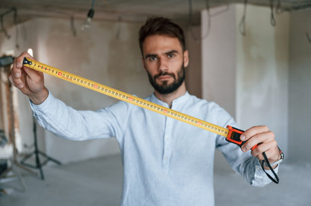 Holding ruler measurement tool. The man is making repairs in the apartment.