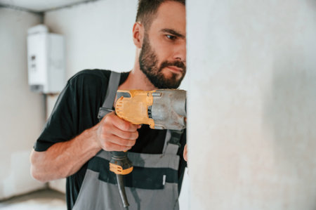 Drilling the hole in wall. The man is making repairs in the apartment.