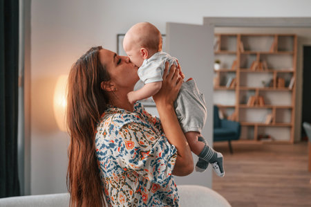 Holding child in the hands. Beautiful happy mother with her newborn son is at home.の写真素材