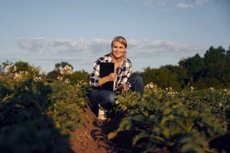 Sitting with notepad and smiling. Woman is on the agricultural field at daytime.