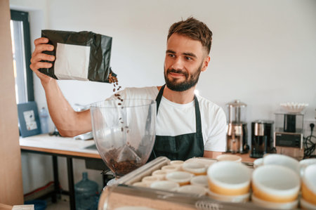 Pours whole coffee beans. Cafe worker in white shirt and black apron is indoors.