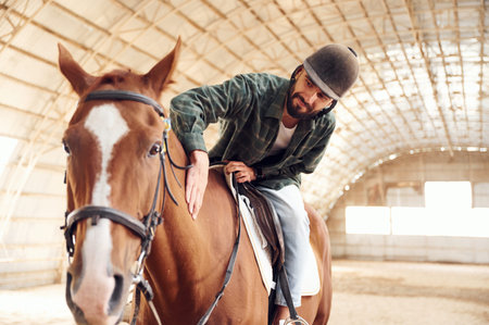 Jockey is in the saddle. Young man with a horse is in the hangar.