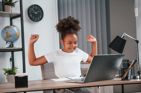 Celebrating success. Passes the exam. Cute female african american student child is sitting by the...