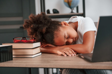Sleeping by leaning on the table. Feeling tired. Cute female african american student child is...
