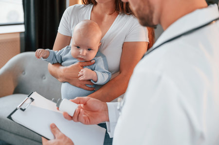 With a prescription. Male doctor is taking care of woman's newborn baby indoors.