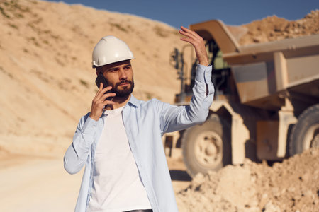 Talking by phone. Man in uniform is working in the quarry at daytime.