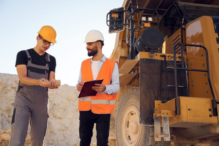 Holding and showing rock that is in the hand. Two men in uniform are working together in the quarry.の写真素材
