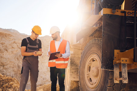 Holding and showing rock that is in the hand. Two men in uniform are working together in the quarry.