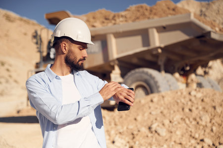 Looking at the watches. Man in uniform is working in the quarry at daytime.