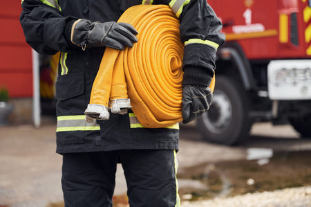 Outside near truck and with fire hose in hands. Woman in uniform is at work in department.