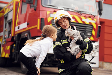 Near the truck. With scottish fold cat. Firefighter woman in uniform is with a little girl.