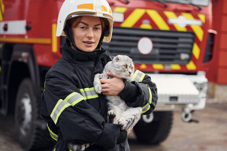 Conception of savior. Holding cat in hands. Woman firefighter in uniform is at work in department.