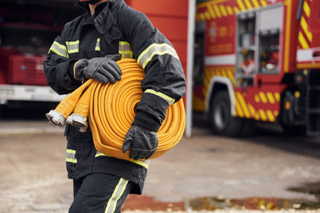 Outside near truck and with fire hose in hands. Woman in uniform is at work in department.