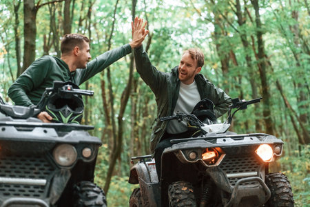 Giving high fives by the hands. Two male atv riders is in the forest together.の写真素材
