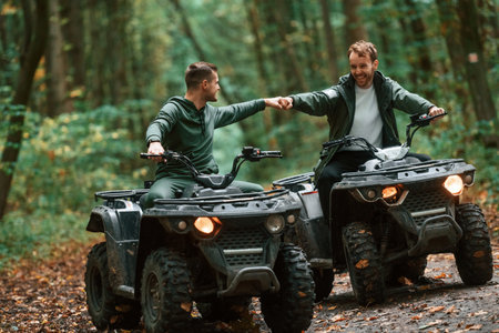 Knocking fists, gesture. Two male atv riders is in the forest together.の写真素材