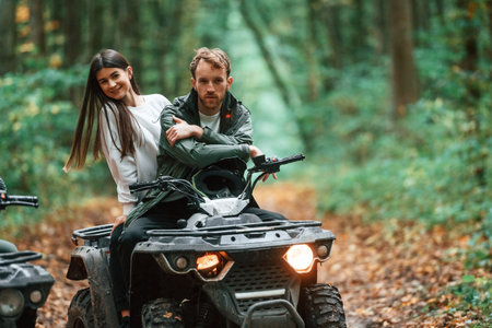 Man is handling the transport. Young couple riding a quad bike in the forest.