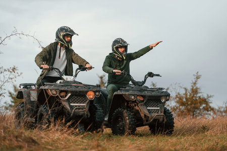 Showing the path by a hand. Two men are on the quad bikes outdoors on the field.
