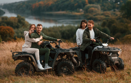 Making a selfie by smartphone. Two young couples with quad bikes is together on the field.の写真素材