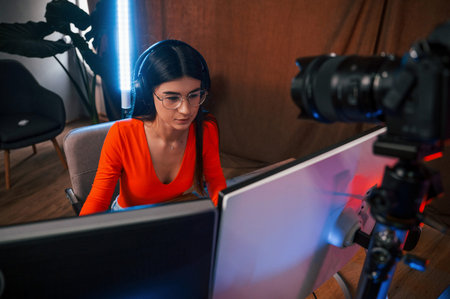 Professional camera is recording the woman. Young beautiful game streamer is indoors with pc.