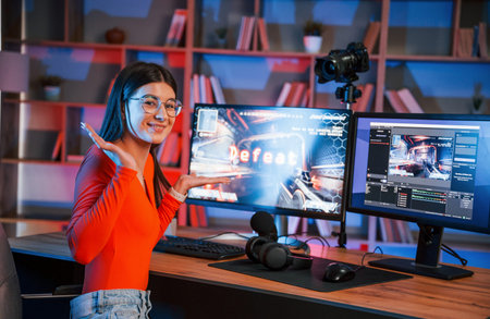 Positive facial expression. Young beautiful game streamer is indoors with pc.