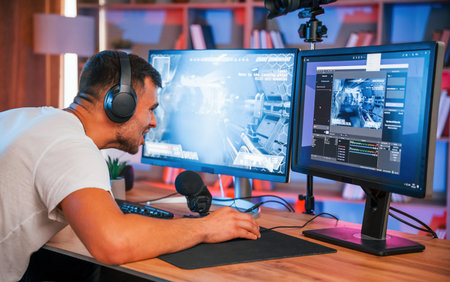 Playing first person shooting game. Male streamer in casual clothes is indoors with pc.