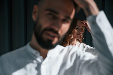 Man is in front of woman. Beautiful young couple is standing together against dark green background.
