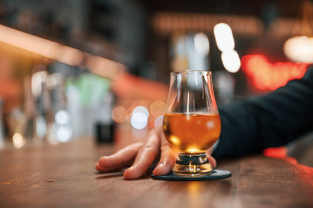 Close up view of glass with drink that is holding by man's hand. In the bar.