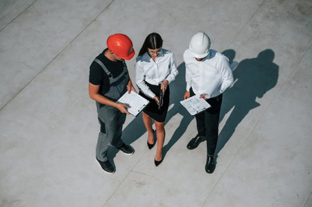 Using documents. Top view of men and woman that are on construction site, working together on the...