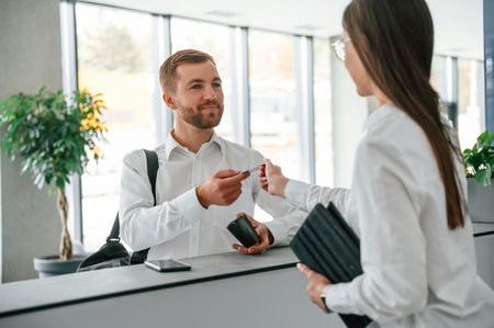 Assistant helping customer. Man in white shirt is ordering a room in the hotel by woman's help.