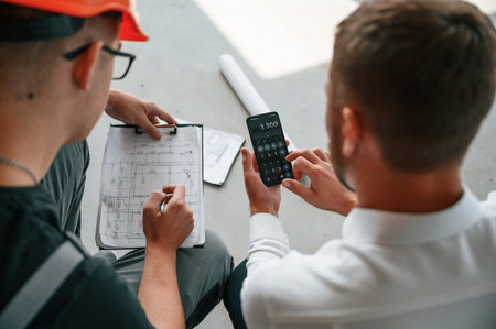 Sitting, using calculator. Manager with foreman are working on the construction site together.