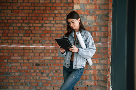 Notepad in hands. Young woman is standing in the unfinished building on construction site and...