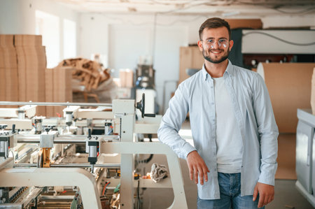 Handsome man is standing and smiling. Print house worker in white clothes is indoors.
