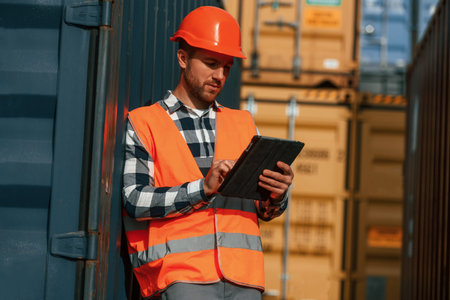 With digital tablet in hands. Male worker is on the location with containers.