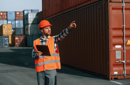Giving instructions by the hand. Male worker is on the location with containers.