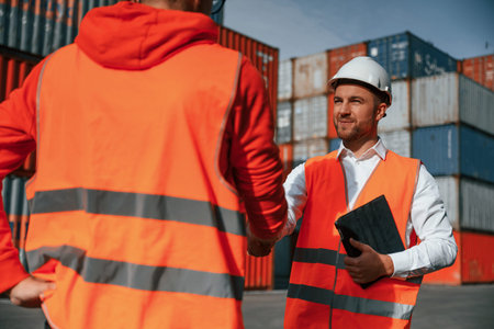 Making handshake. Two male workers is on the location with containers.