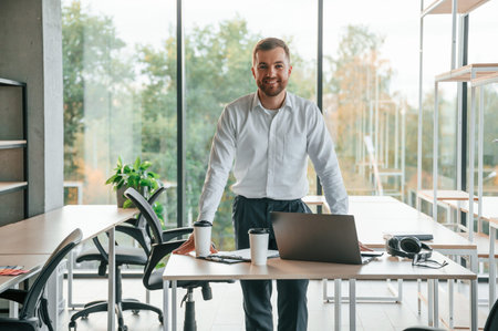 Standing and smiling. Man in formal clothes is working in the modern office.