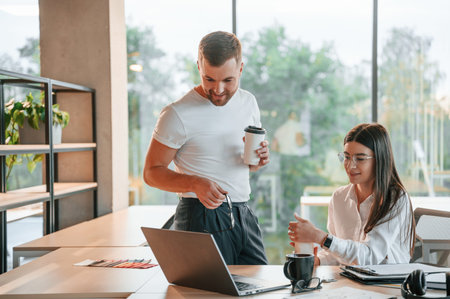 Working by using laptop. Man and woman are in the modern office together.