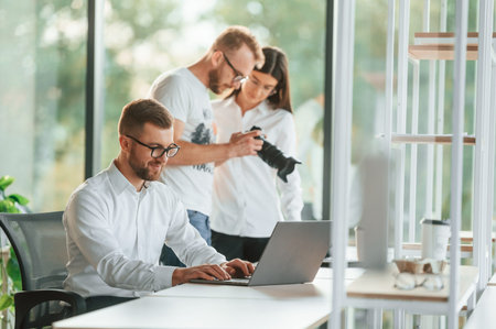 Man showing photos on the camera to a woman. Three people in formal clothes are working in the...